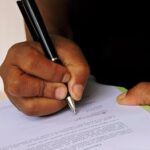 Person signing a document with a pen, emphasizing professionalism and formality.