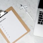 A clean and organized office desk setup featuring a laptop, clipboard with application form, and pen.