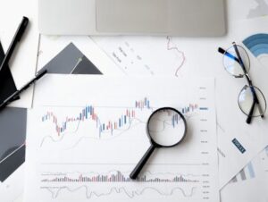 Flat lay of stock market analysis documents with magnifying glass, pens, and glasses.
