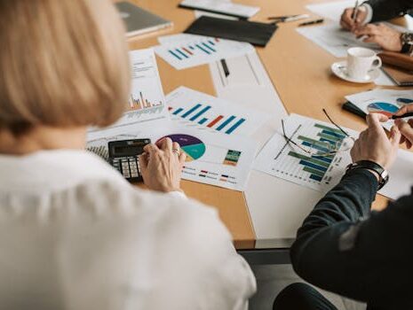 Overhead view of professionals discussing financial graphs and using calculators in an office setting.
